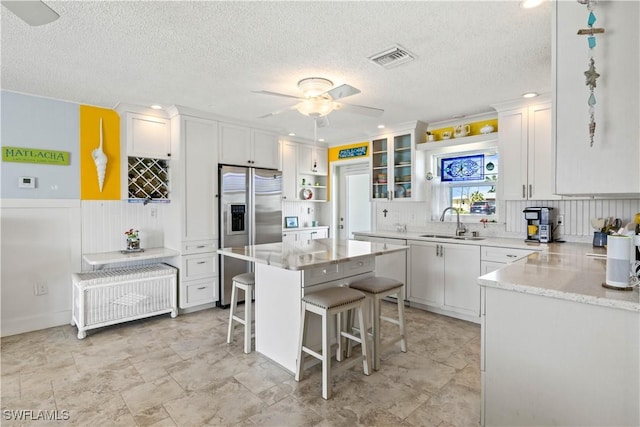 kitchen with a sink, visible vents, a kitchen breakfast bar, white cabinetry, and stainless steel fridge