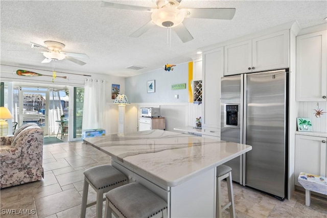 kitchen with white cabinets, a center island, a kitchen breakfast bar, and stainless steel fridge with ice dispenser