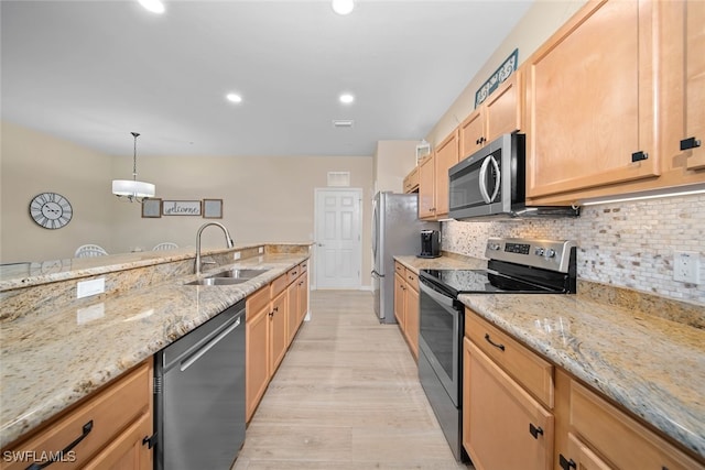 kitchen with appliances with stainless steel finishes, sink, hanging light fixtures, light hardwood / wood-style floors, and light stone counters