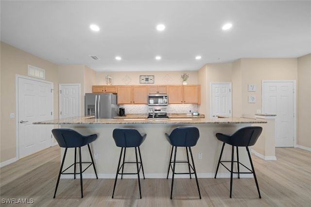 kitchen featuring a large island with sink, stainless steel appliances, light brown cabinetry, and light hardwood / wood-style floors