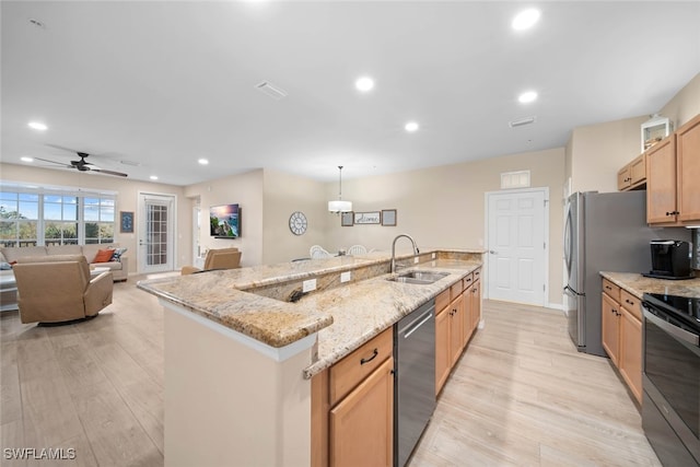 kitchen featuring a large island with sink, light hardwood / wood-style flooring, hanging light fixtures, stainless steel appliances, and sink