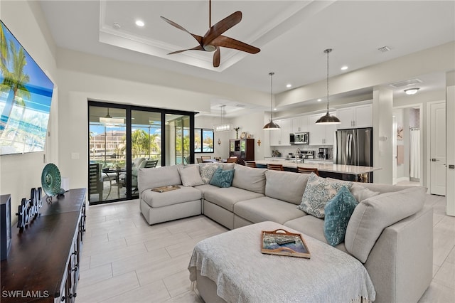 living room featuring a raised ceiling, ceiling fan, and crown molding