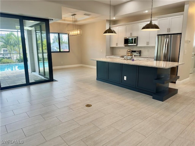 kitchen with light stone countertops, stainless steel appliances, sink, white cabinetry, and hanging light fixtures