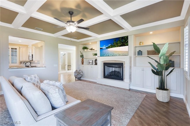 living room featuring built in features, dark hardwood / wood-style flooring, coffered ceiling, ceiling fan, and beam ceiling