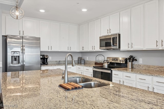 kitchen featuring stainless steel appliances, white cabinetry, sink, light stone countertops, and decorative light fixtures