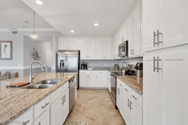 kitchen featuring stainless steel appliances, pendant lighting, sink, light stone countertops, and white cabinetry