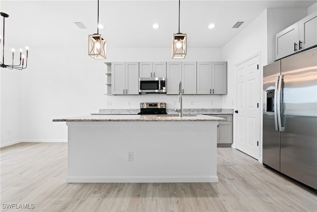 kitchen with pendant lighting, stainless steel appliances, and an island with sink