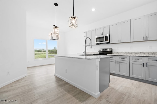 kitchen with stainless steel appliances, sink, light stone countertops, a kitchen island with sink, and light wood-type flooring