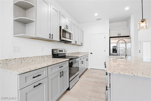 kitchen featuring light stone countertops, appliances with stainless steel finishes, decorative light fixtures, and light hardwood / wood-style flooring