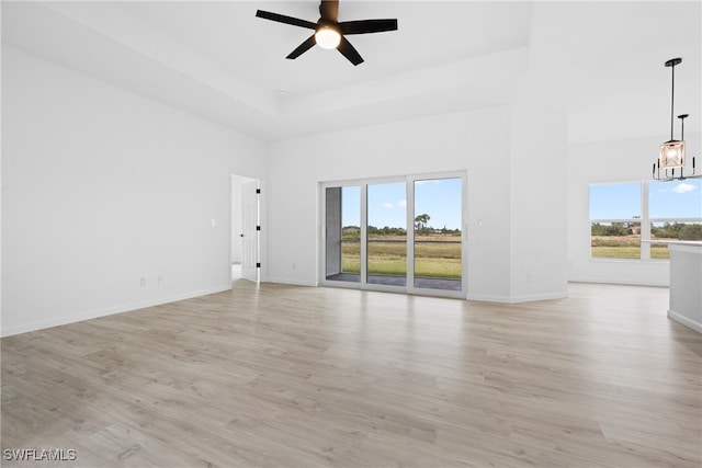 unfurnished living room with a towering ceiling, ceiling fan with notable chandelier, plenty of natural light, and light hardwood / wood-style flooring