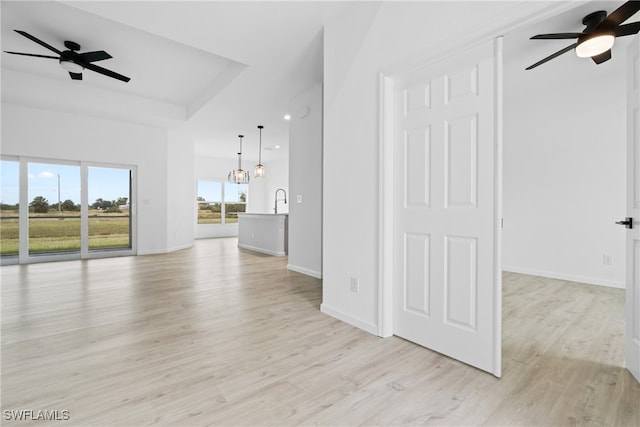 unfurnished living room with sink, ceiling fan with notable chandelier, and light hardwood / wood-style flooring