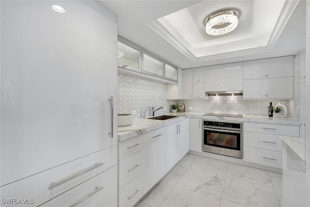 kitchen featuring oven, white cabinetry, sink, and a tray ceiling