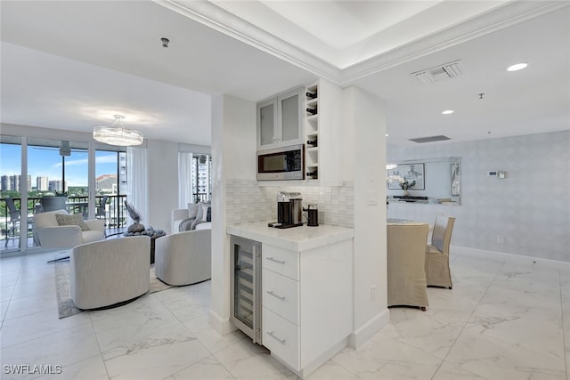 kitchen featuring white cabinetry, stainless steel microwave, wine cooler, a notable chandelier, and decorative backsplash