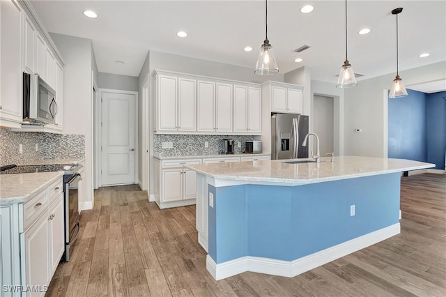 kitchen featuring white cabinets, hanging light fixtures, a center island with sink, appliances with stainless steel finishes, and light wood-type flooring