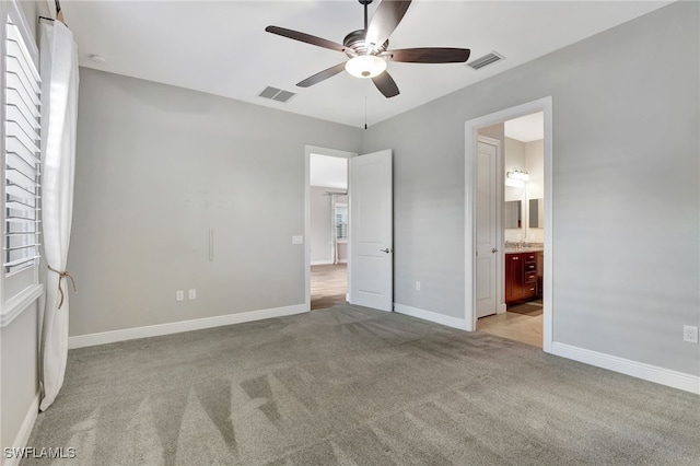 unfurnished bedroom featuring ceiling fan, light carpet, and ensuite bath