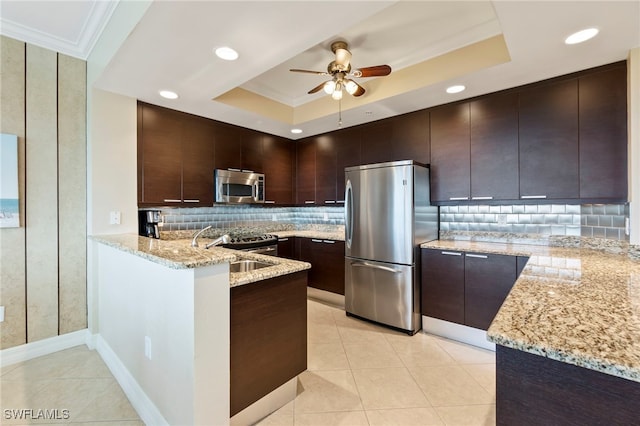 kitchen featuring dark brown cabinets, appliances with stainless steel finishes, light stone countertops, and a raised ceiling