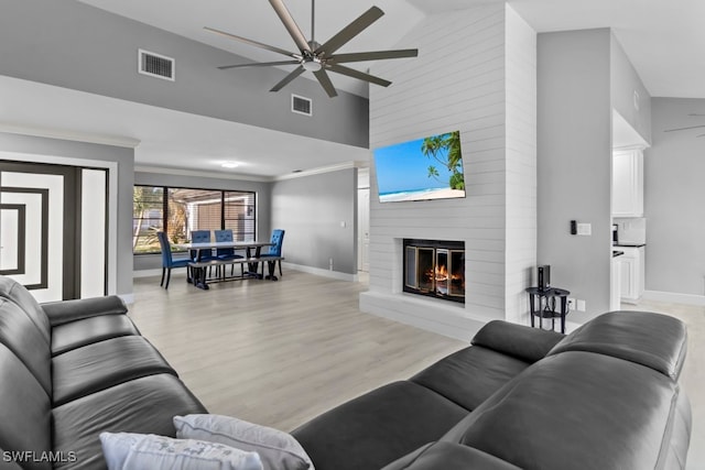 living room with ceiling fan, light hardwood / wood-style floors, a fireplace, and high vaulted ceiling