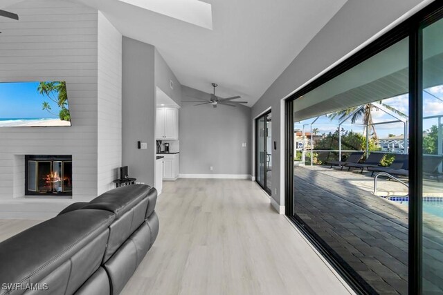 living room featuring ceiling fan, a fireplace, high vaulted ceiling, and light wood-type flooring