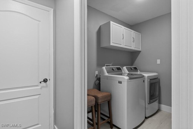 laundry area with cabinets, washing machine and dryer, and light hardwood / wood-style flooring