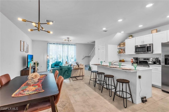 kitchen with a center island with sink, a kitchen breakfast bar, white cabinetry, and appliances with stainless steel finishes