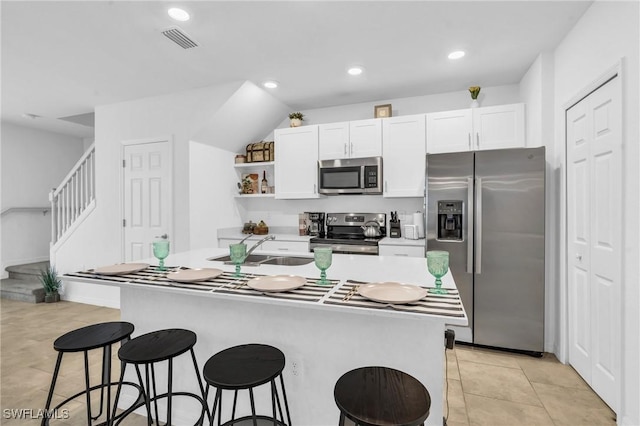 kitchen with white cabinets, a kitchen bar, stainless steel appliances, and an island with sink