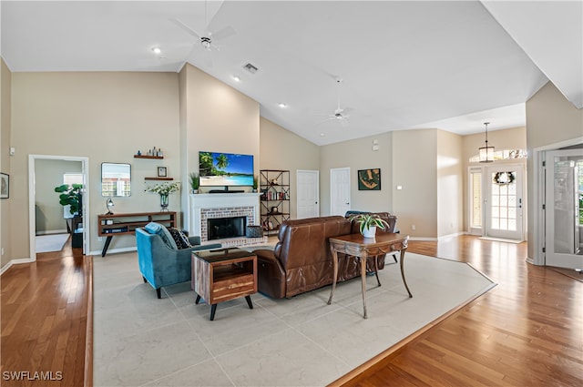 living room with ceiling fan, a fireplace, light hardwood / wood-style floors, and high vaulted ceiling