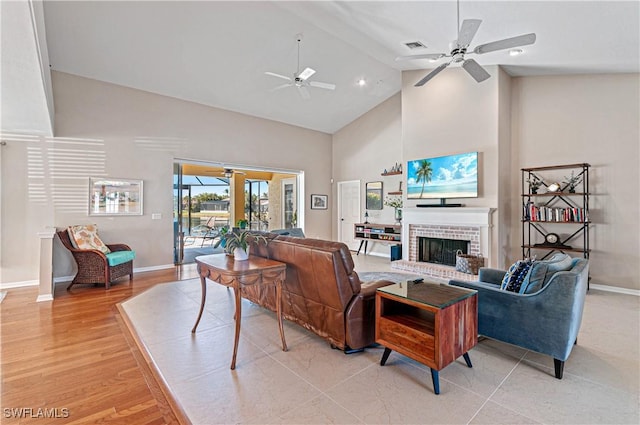 living room with ceiling fan, a fireplace, high vaulted ceiling, and light hardwood / wood-style flooring