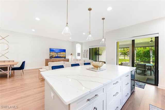 kitchen featuring a kitchen island, pendant lighting, white cabinets, light stone counters, and light hardwood / wood-style flooring