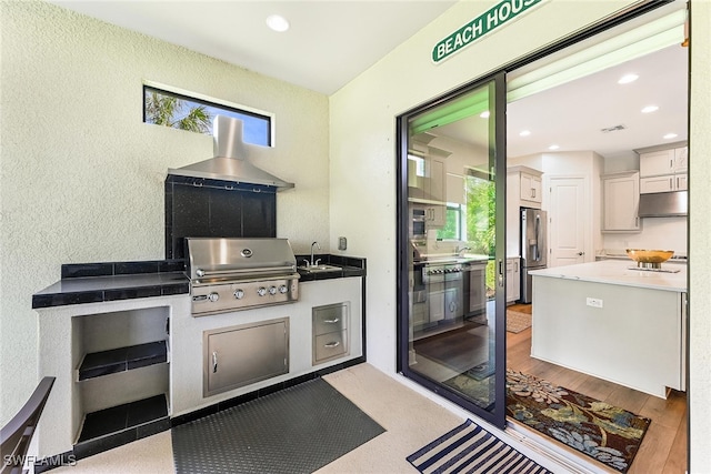 kitchen with wall chimney range hood, white cabinetry, light wood-type flooring, stainless steel refrigerator with ice dispenser, and sink