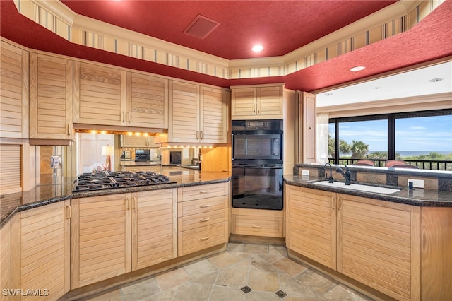 kitchen featuring sink, light brown cabinets, dark stone counters, stainless steel gas stovetop, and double oven