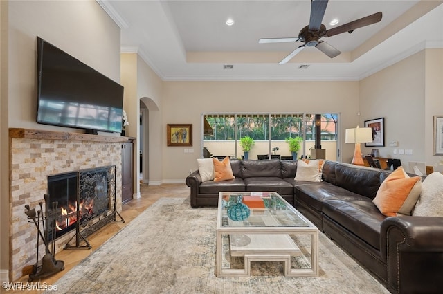 living room with ceiling fan, ornamental molding, a tile fireplace, and a tray ceiling