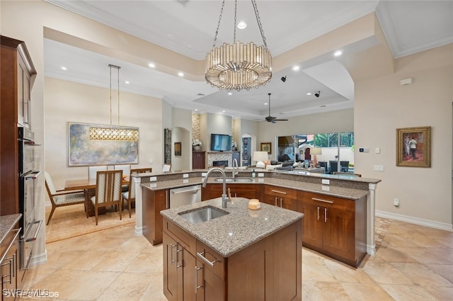 kitchen featuring a center island with sink, ceiling fan with notable chandelier, sink, decorative light fixtures, and light stone counters