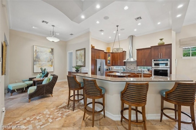 4908 Rustic Oaks Cir, Naples, FL 34105 - kitchen featuring wall chimney range hood, stainless steel appliances, a kitchen breakfast bar, ornamental molding, and pendant lighting