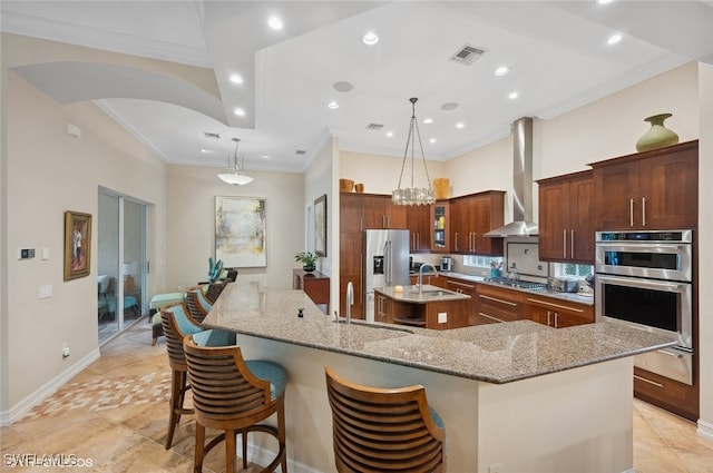 kitchen featuring a kitchen bar, appliances with stainless steel finishes, wall chimney exhaust hood, a spacious island, and pendant lighting