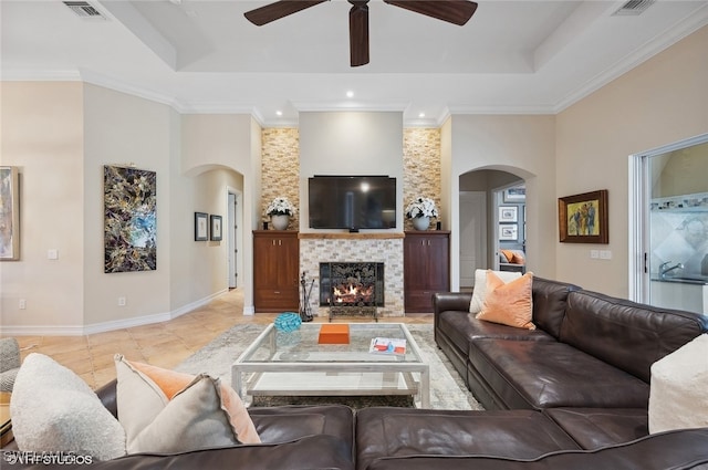 tiled living room featuring a high ceiling, a raised ceiling, ceiling fan, ornamental molding, and a fireplace