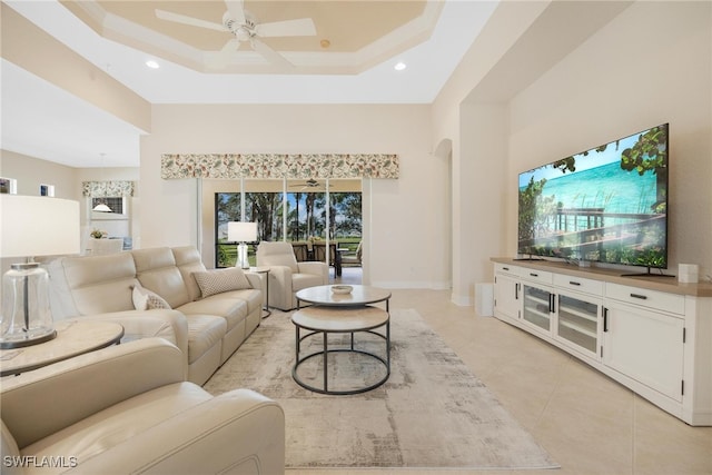 living room with a raised ceiling, ceiling fan, light tile patterned flooring, and a high ceiling