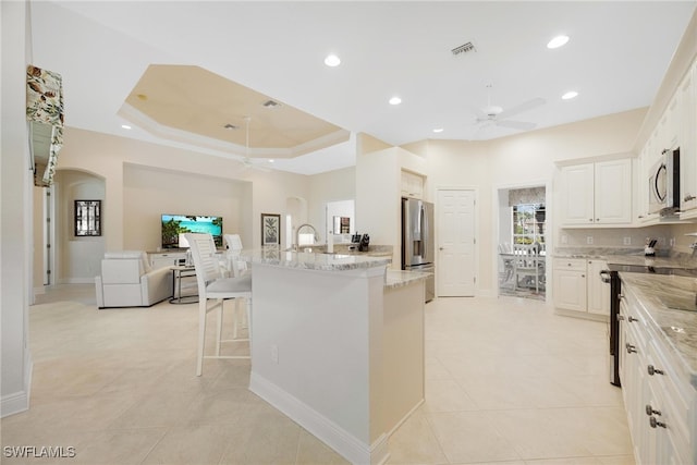 kitchen featuring white cabinets, a breakfast bar area, an island with sink, light stone counters, and stainless steel appliances