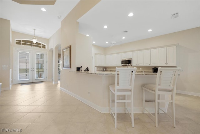 kitchen with kitchen peninsula, french doors, light stone countertops, white cabinets, and a breakfast bar area