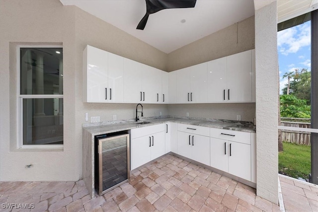 kitchen featuring light stone countertops, sink, white cabinetry, and beverage cooler