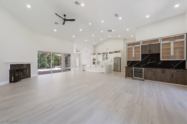 unfurnished living room featuring ceiling fan, light wood-type flooring, high vaulted ceiling, and beverage cooler