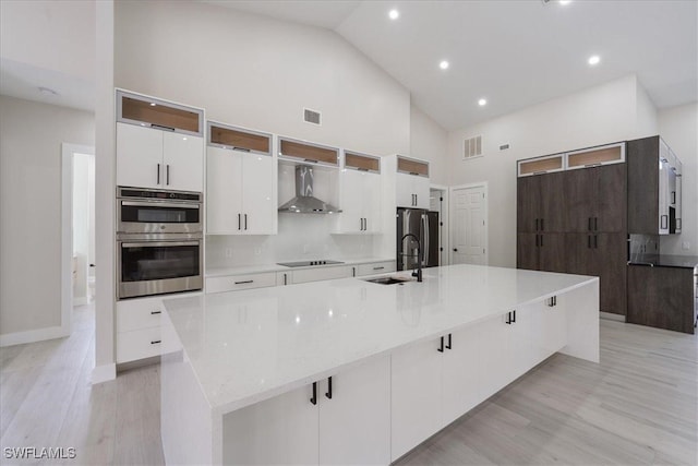 kitchen featuring a spacious island, high vaulted ceiling, wall chimney exhaust hood, and appliances with stainless steel finishes