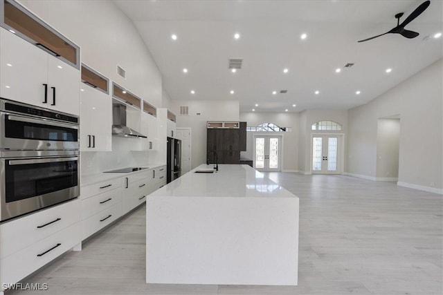 kitchen with wall chimney exhaust hood, a large island with sink, sink, french doors, and stainless steel appliances