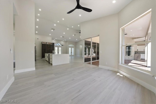 unfurnished living room with light hardwood / wood-style floors, a towering ceiling, and ceiling fan