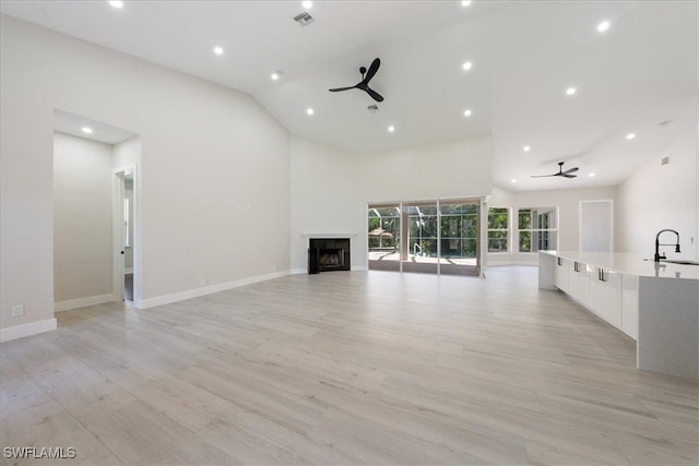 unfurnished living room featuring light hardwood / wood-style flooring, high vaulted ceiling, sink, and ceiling fan