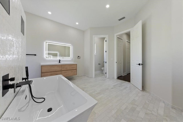 bathroom featuring a tub to relax in, vanity, and toilet