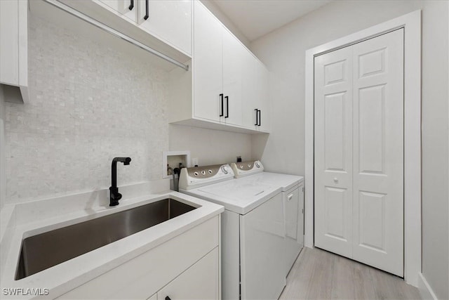 laundry area with sink, independent washer and dryer, light hardwood / wood-style floors, and cabinets