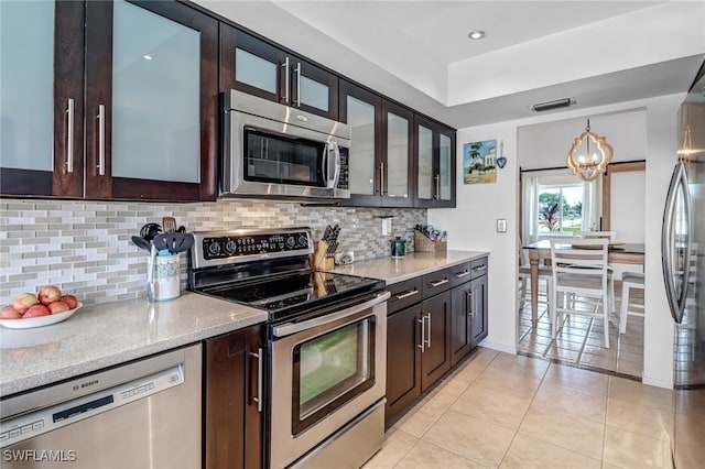 kitchen featuring light stone countertops, dark brown cabinets, stainless steel appliances, and light tile patterned flooring