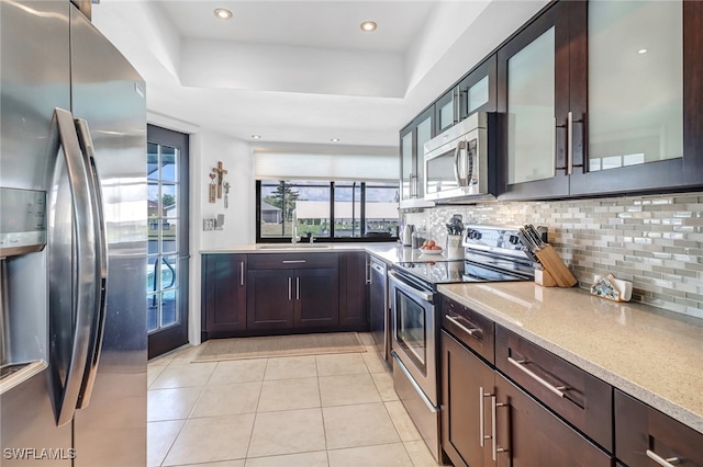 kitchen featuring tasteful backsplash, light stone countertops, a raised ceiling, and appliances with stainless steel finishes