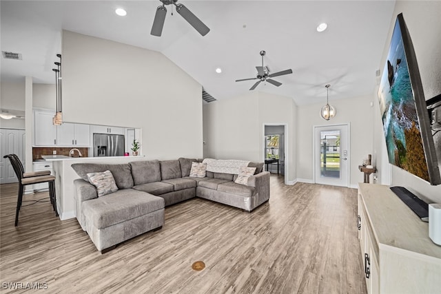 living room with ceiling fan, light hardwood / wood-style floors, and high vaulted ceiling