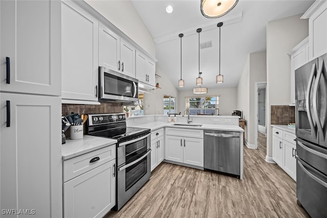 kitchen featuring kitchen peninsula, appliances with stainless steel finishes, sink, hanging light fixtures, and lofted ceiling